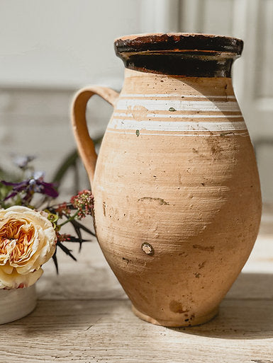 A close up view of a vintage terracotta jug from Hungary. The vintage pot has white stripes around the neck and a black glaze around the rim.