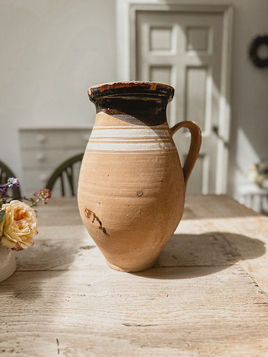 An antique hungarian pot is sat on a rustic wooden table. Sunlight is streaming down from windows above.