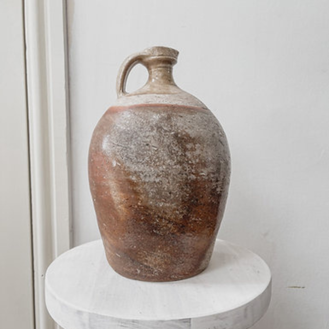 Antique french stoneware flagon with a marble-like colouring on top of a whitewashed stool and neutral walls